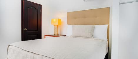 Una camera d'albergo con un letto, un comodino, una lampada, un condizionatore d'aria e una porta.