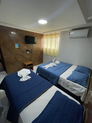 A hotel room with two beds, a TV mounted on the wall, an air conditioning unit, and a small wooden table.