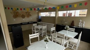Un espace repas avec des tables et des chaises blanches, un distributeur d’eau et des œuvres d’art décoratives sur les murs.