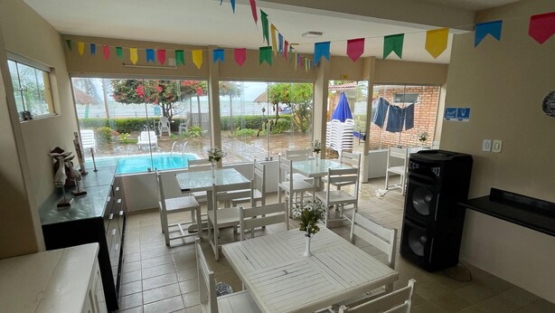 Un espace repas avec des tables et des chaises blanches, une piscine visible à travers de grandes fenêtres et des drapeaux colorés suspendus au plafond.