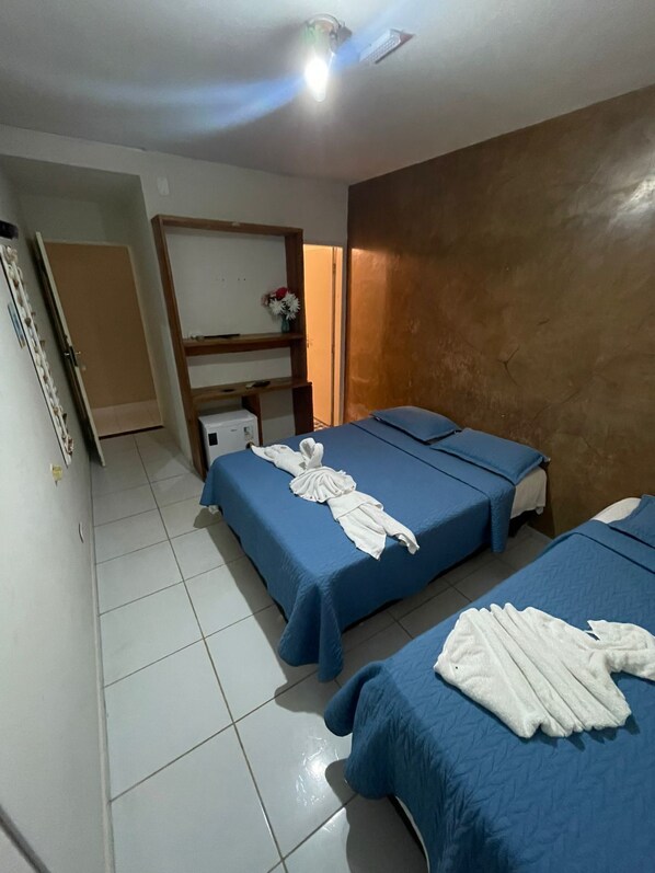 A hotel room with two beds, a wooden shelf with a vase, and a white refrigerator. - Pousada Solmar (Japaratinga)