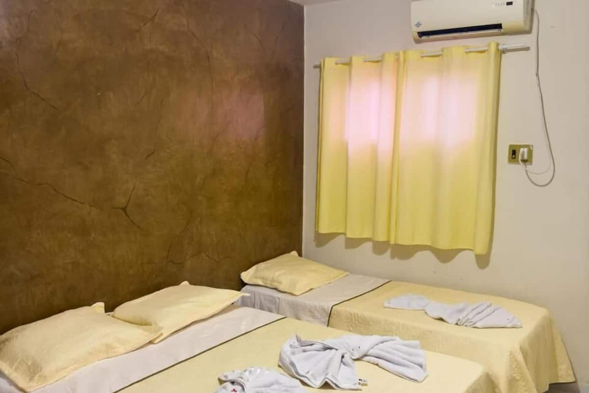 Een hotelkamer met twee bedden, een plafondventilator, een airconditioner en een geel gordijn.