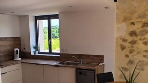 Een moderne keuken met een ingebouwde vaatwasser, een raam met uitzicht op groen, en een eethoek met een ronde tafel en stoelen.
