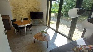 Een eetgedeelte met een ronde tafel, stoelen, een televisie en een potplant.