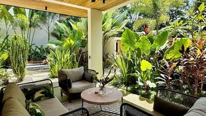 Ein Innenhof mit Sitzgelegenheiten, darunter eine Couch und Stühle, umgeben von Pflanzen und einem Deckenventilator.
