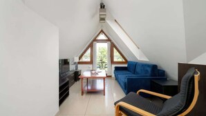 Ein modernes Schlafzimmer im Loft-Stil mit schrägverdeckter Decke, einem Bettgestell aus Holz, einem blauen Sofa und einem Holzstuhl.