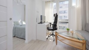 A modern room with a bed, a desk with a computer, a glass table, and a sofa.