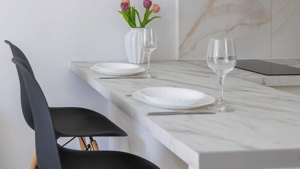A dining area with a marble countertop, two black chairs, a vase with flowers, and a white plate.