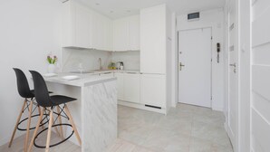 A modern kitchen with white cabinets, a marble countertop, and two black chairs.