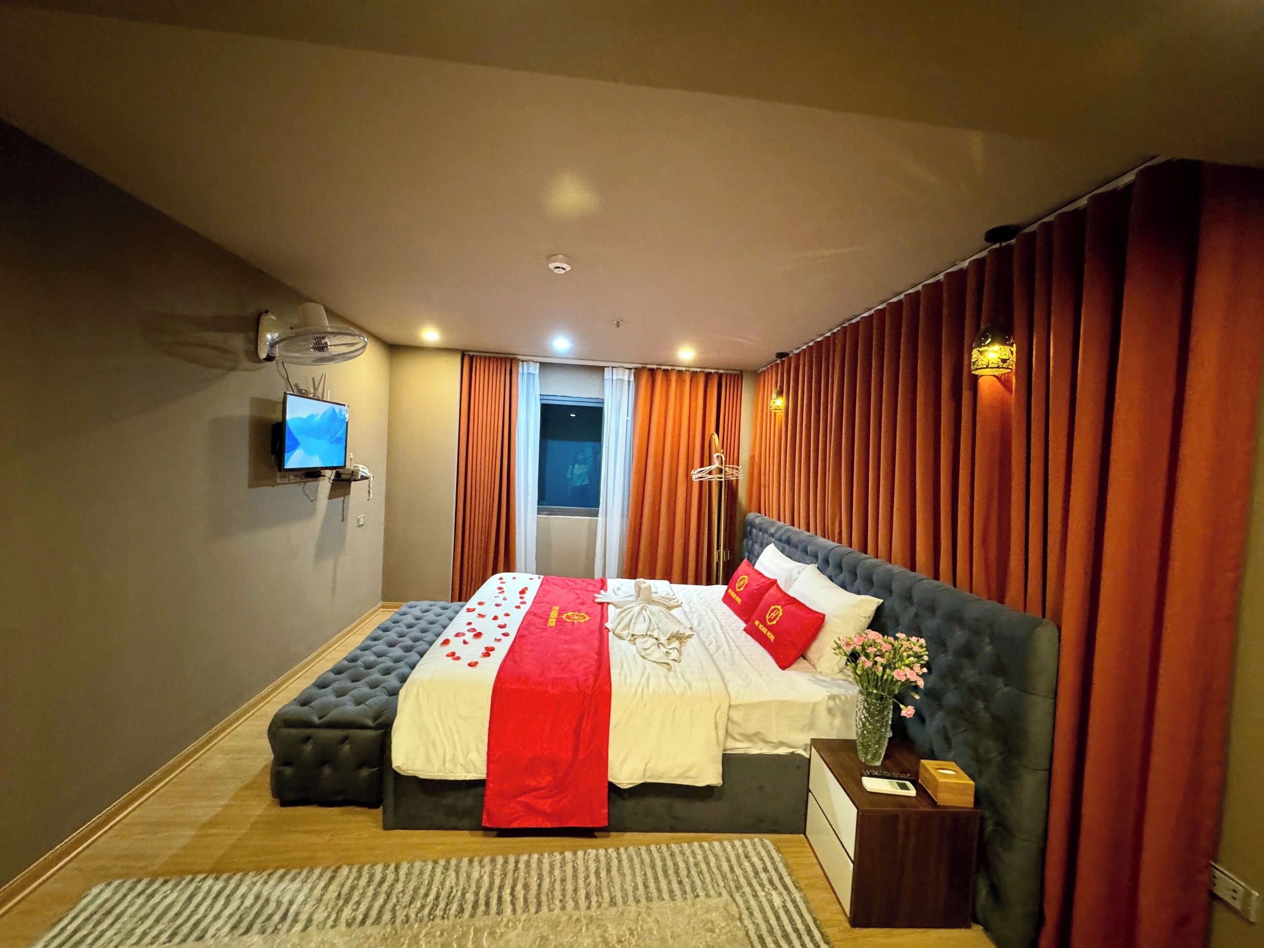 Een hotelkamer met een groot bed, een flatscreen-tv, een nachtkastje en een raam met gordijnen.
