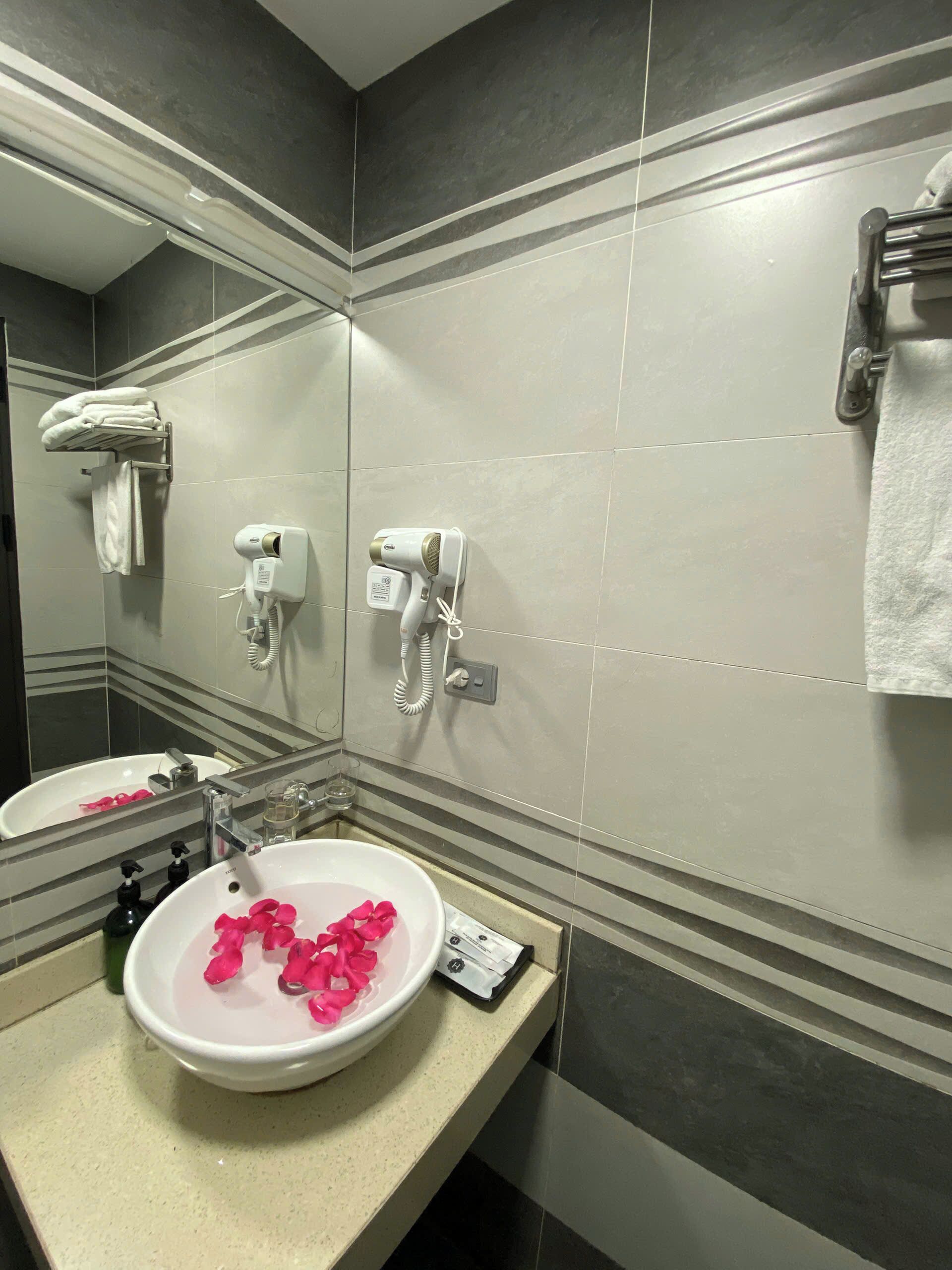A bathroom with a sink, mirror, towel rack, and hair dryers.