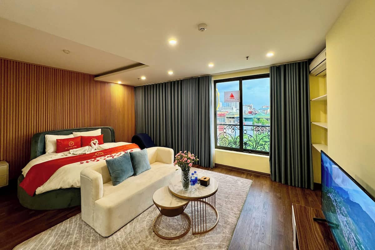A modern hotel room with a bed, a sofa, a coffee table, and a TV.