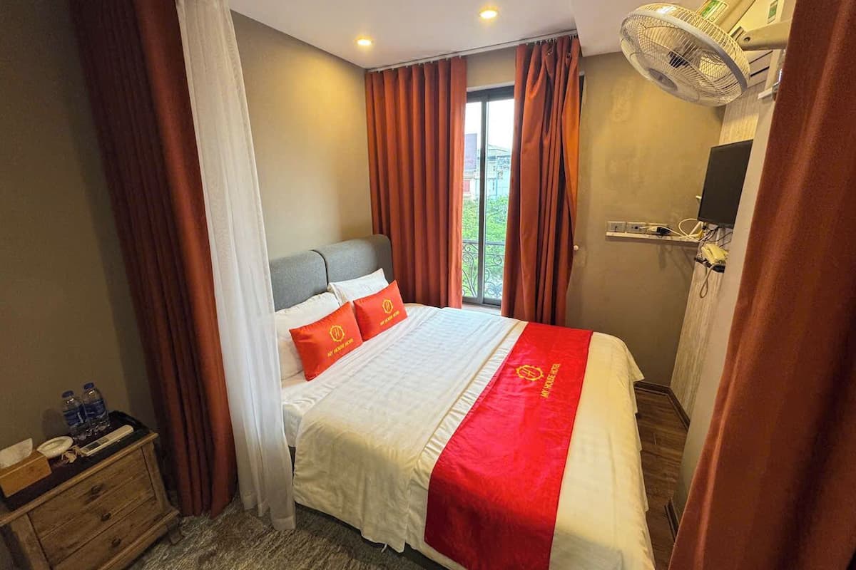 A hotel room with a bed, a nightstand, a desk, and a window with curtains.