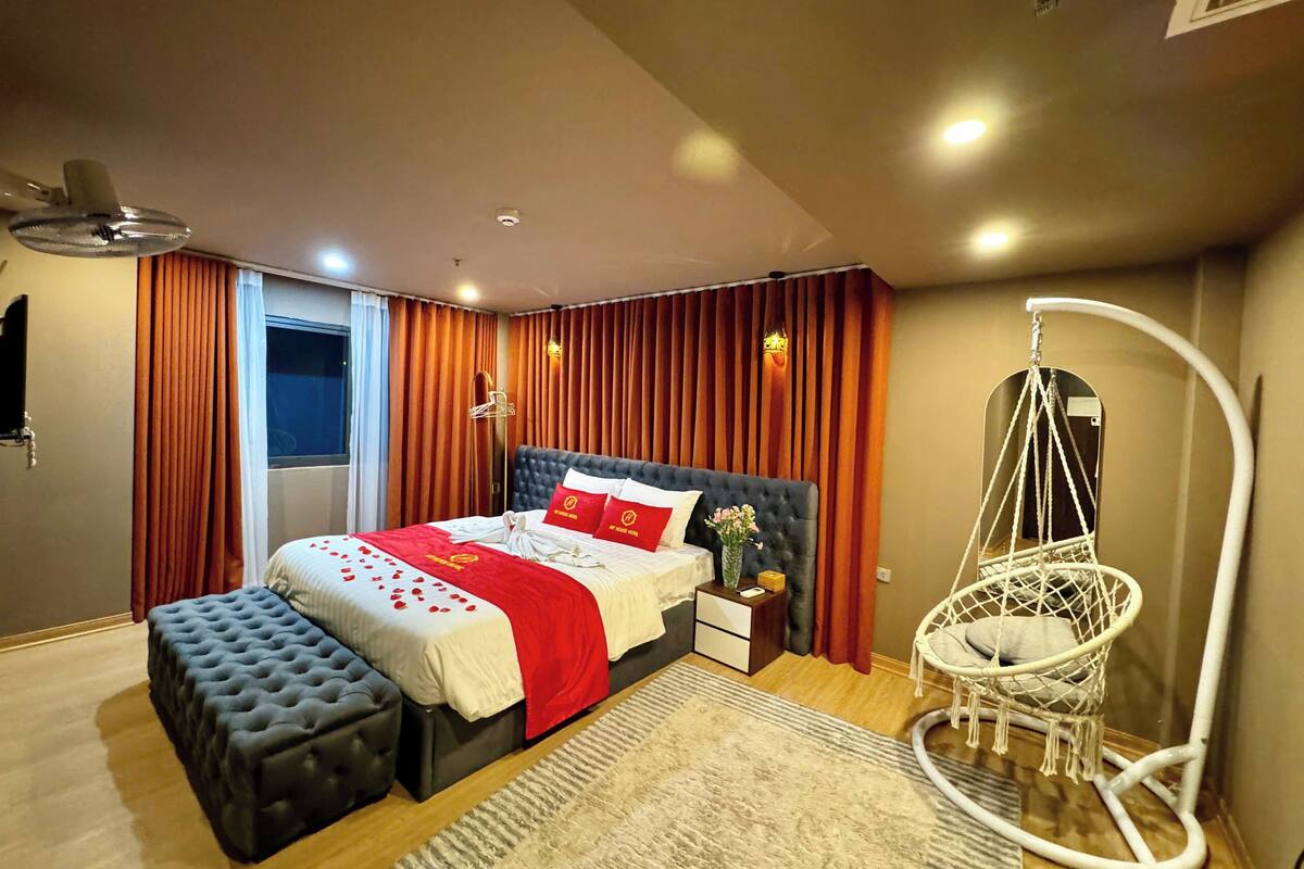 A modern bedroom with a large bed, a hanging chair, and a window with curtains.