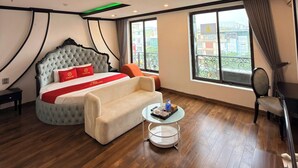 Un hotel moderno con una cama grande, un sofá, una pequeña mesa redonda y vistas a la ciudad a través de amplios ventanales.