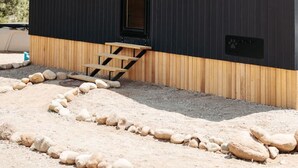 A modern, compact building with a dark exterior, a wooden lower section, and a small front door with a set of wooden steps leading up to it. - Luxurious, Riverside Chalet! Romantic Mountain Views (Johnson Village)