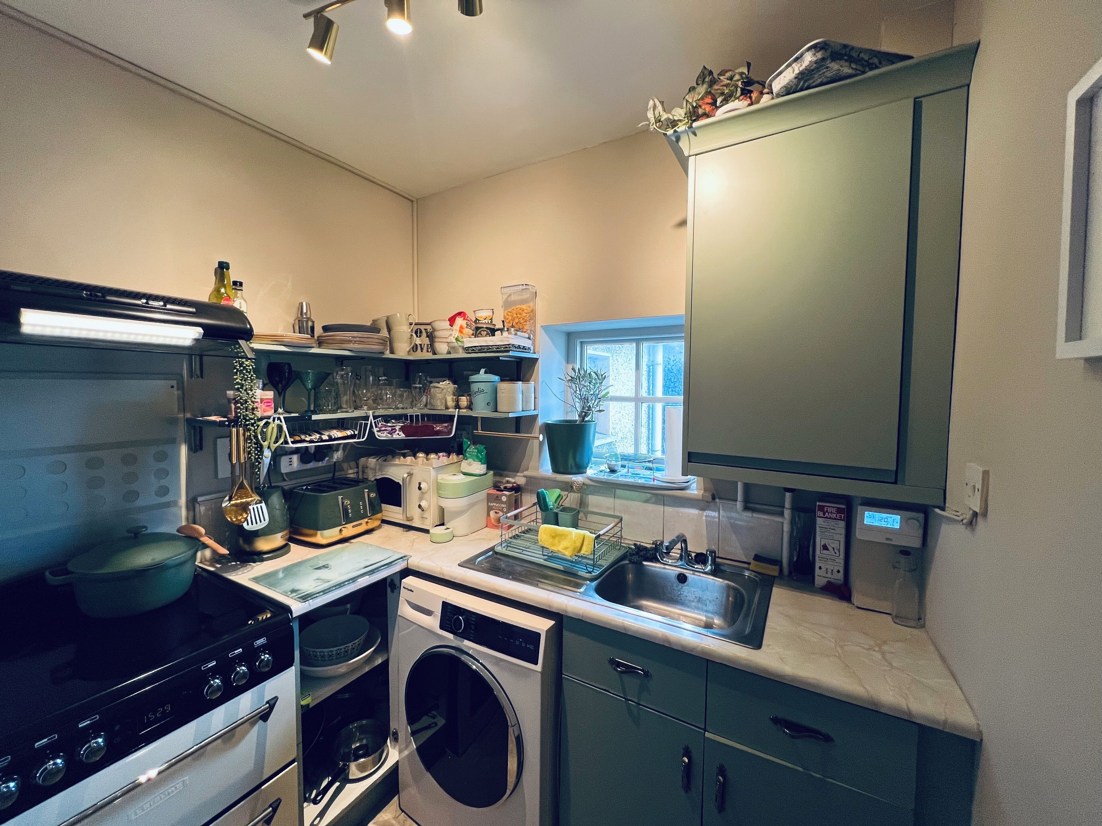 A compact kitchen with a stove, oven, washing machine, and a sink.