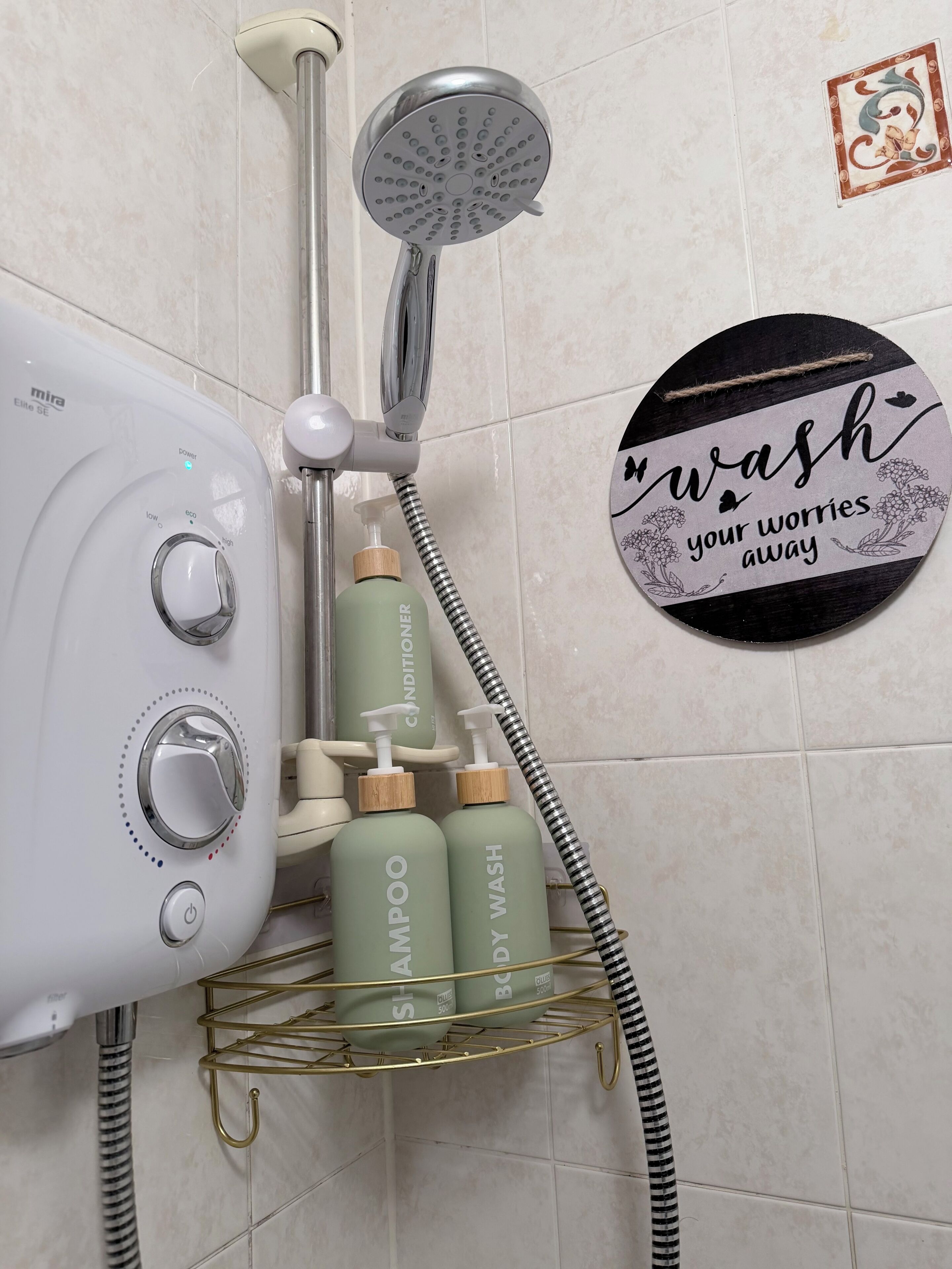 A bathroom with a shower, a Mira Elite 5E hairdryer, and a shelf holding shampoo and body wash bottles.