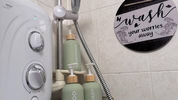 A bathroom with a shower, a Mira Elite 5E hairdryer, and a shelf holding shampoo and body wash bottles.