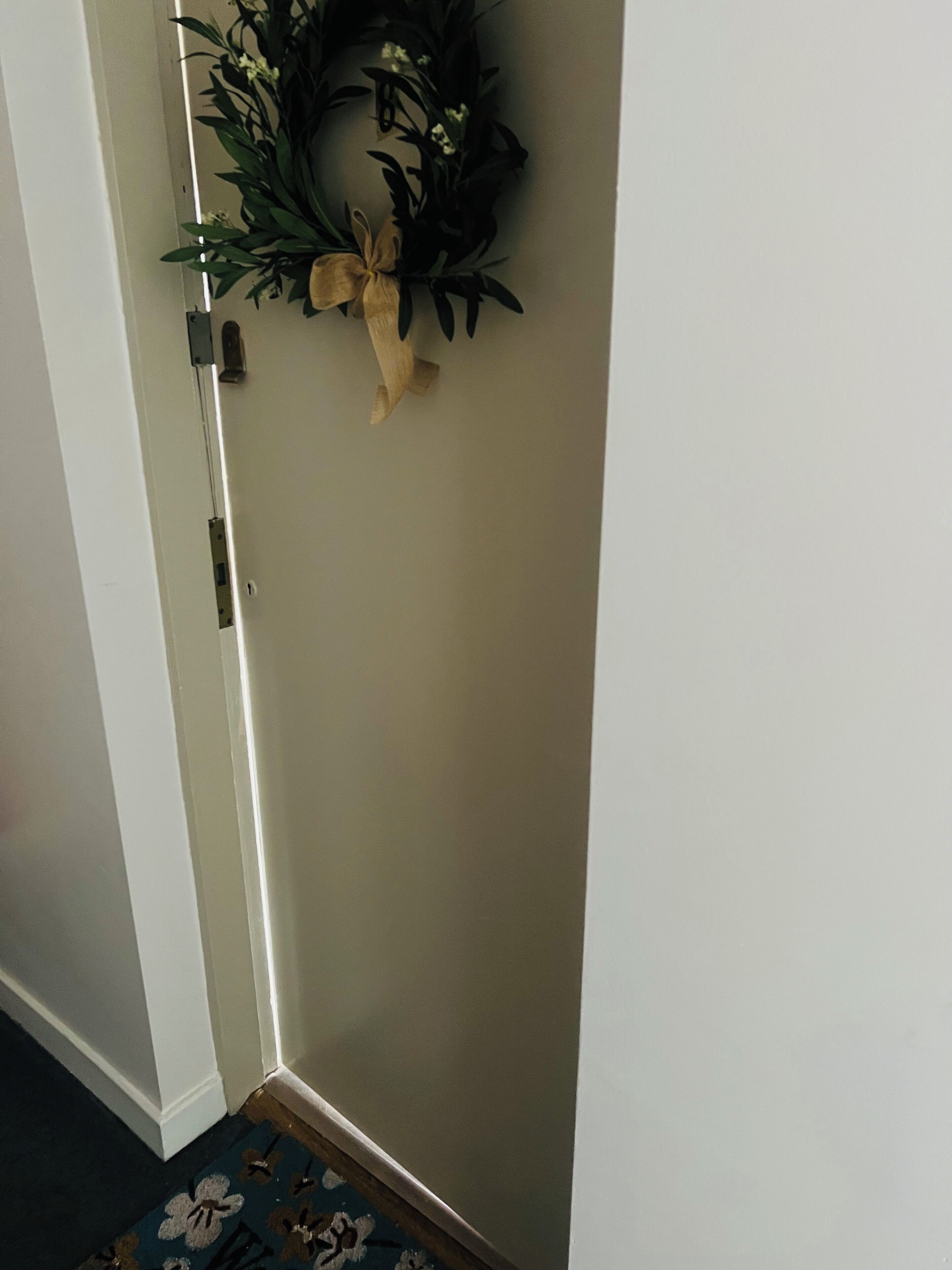 A corner of a room with a door, a light switch, and a wall-mounted wreath.