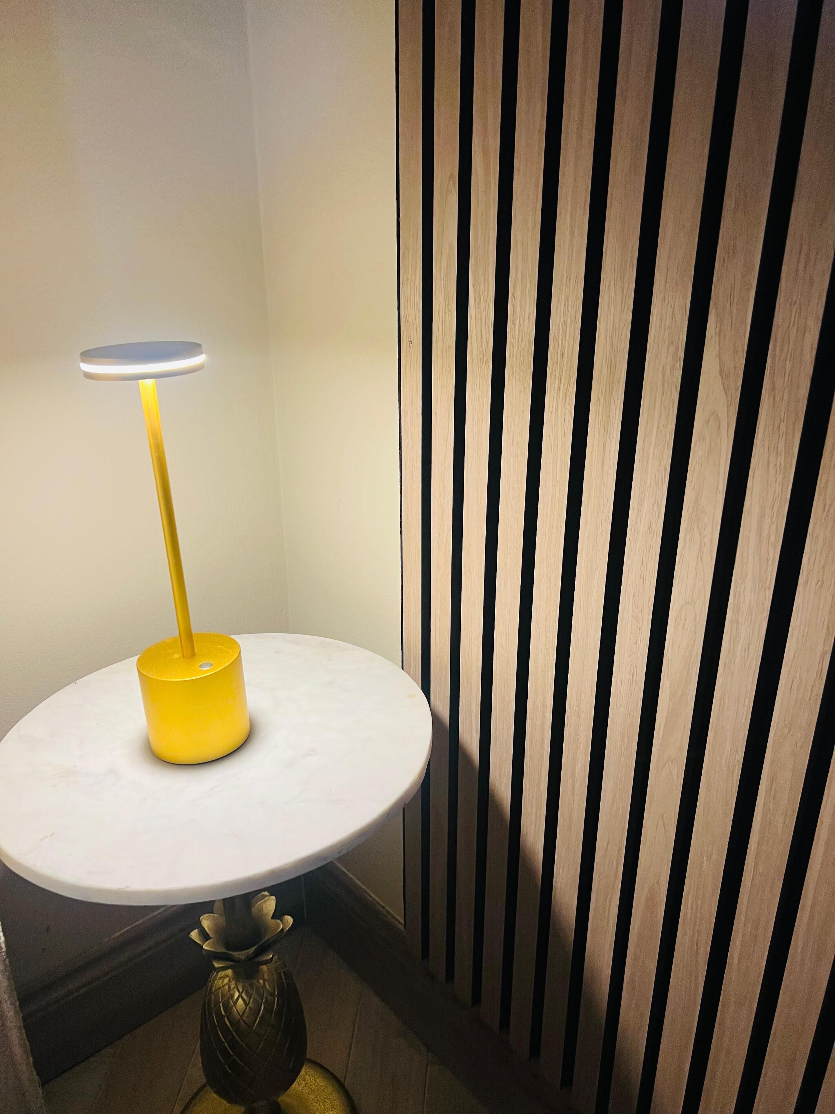 A round table with a yellow base and a white top, positioned against a wall with vertical wooden slats.