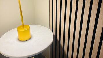 A round table with a yellow base and a white top, positioned against a wall with vertical wooden slats.
