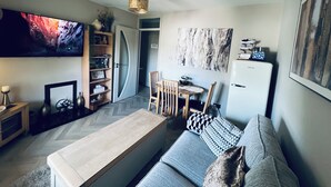 A modern living room with a sofa, a coffee table, a TV, a bookshelf, and a dining area with chairs and a table. - Cosy apartment in heart of Cork City (Cork)