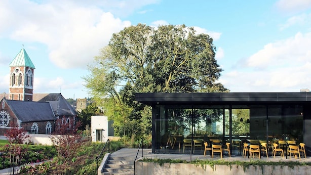 A modern building with a glass facade, outdoor seating area, and a historic church in the background. - Cosy apartment in heart of Cork City (Cork)