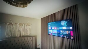 A living room with a flat-screen TV mounted on a wall, a tufted sofa, macramé wall hangings, and a patterned ceiling light. - Cosy apartment in heart of Cork City (Cork)
