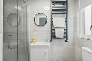 Un bagno moderno con cabina doccia in vetro, lavandino bianco, specchio tondo e porta asciugamani con due asciugamani.