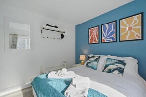 Un dormitorio con una cama, una ventana, un aire acondicionado de pared y tres obras de arte enmarcadas.