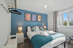 Una camera da letto con un letto, due comodini, una finestra con tende e tre opere d'arte appese al muro.