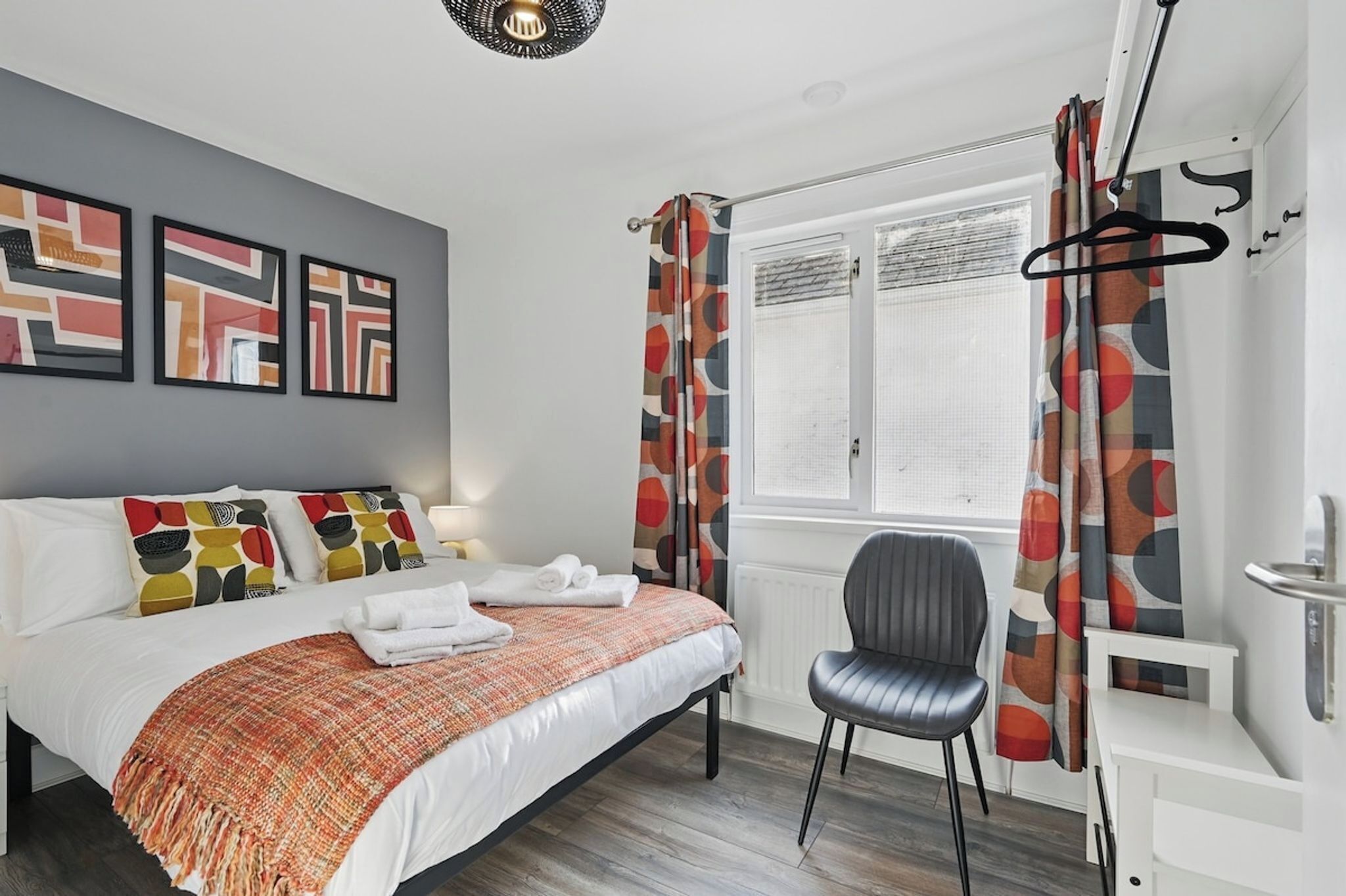 Une chambre bien rangée, avec un lit, une chaise, un bureau et une fenêtre avec des rideaux.