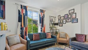 A living room with a blue sofa, two armchairs, a coffee table, and a large window with colorful curtains.