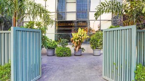 A modern building entrance with a glass facade, potted plants, and a tiled pathway.