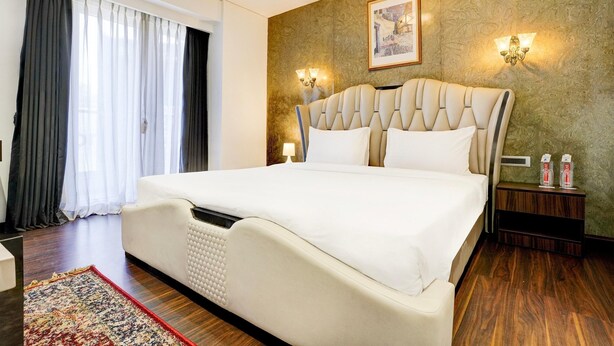 A hotel room with a large bed, a wooden floor, a patterned wall, and two wall-mounted lamps.