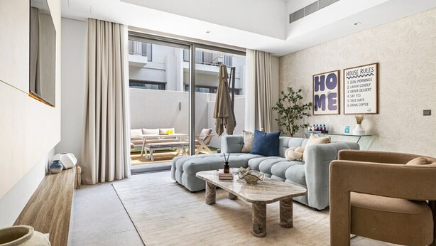 A modern living room with a sofa, a coffee table, and a chair. There is a sliding glass door leading to a balcony.