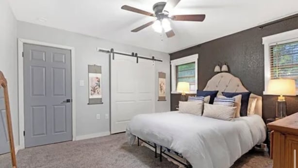 Une chambre à coucher avec un lit, un ventilateur de plafond, une fenêtre avec des stores et une porte.