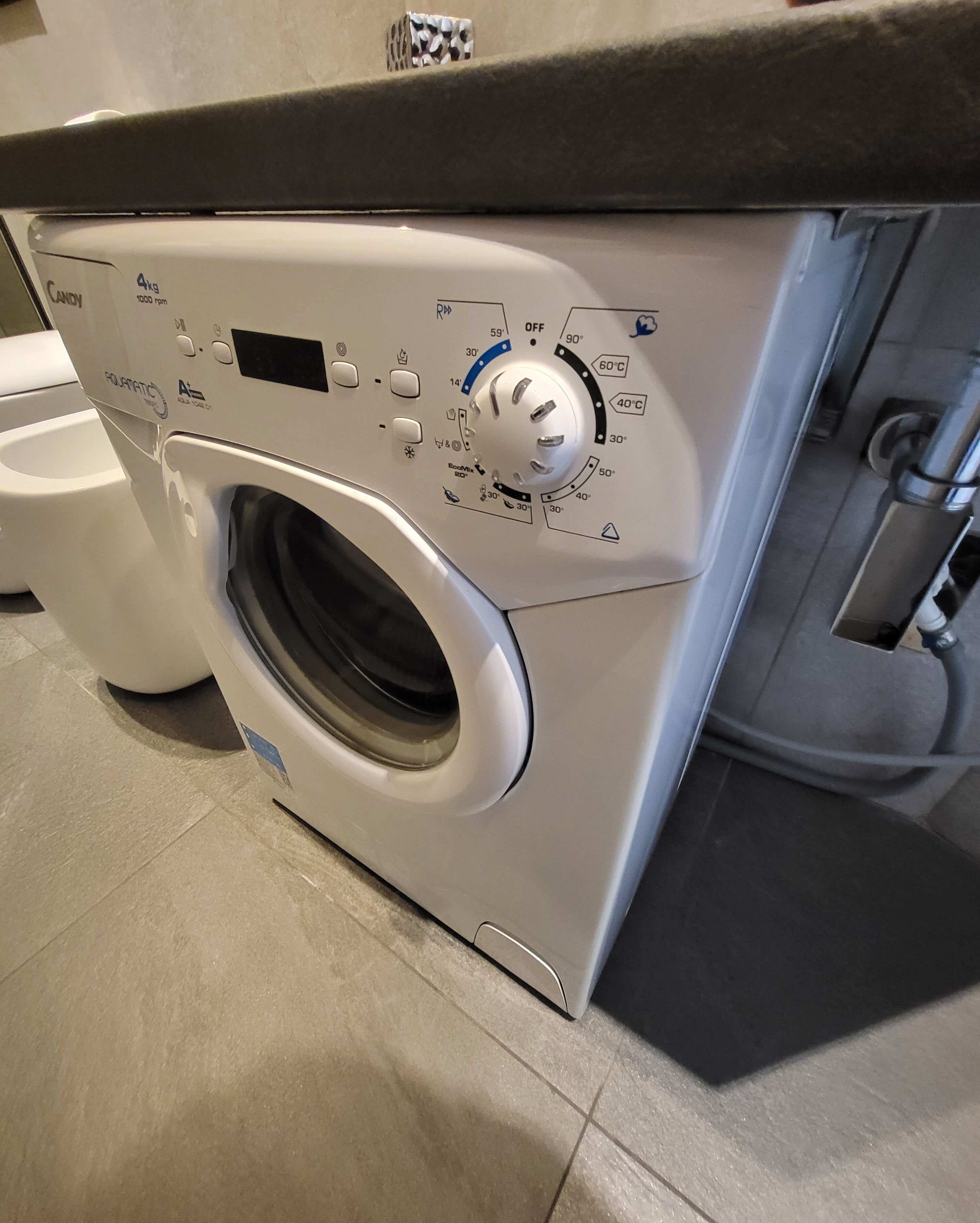 Une machine à laver à chargement frontal dotée d’un panneau de commande numérique, d’un robinet d’arrivée d’eau et d’un tuyau d’évacuation.