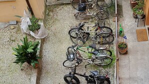 Une cour intérieure où sont garés des vélos le long des murs, entourée de plantes en pot et recouverte de gravier.