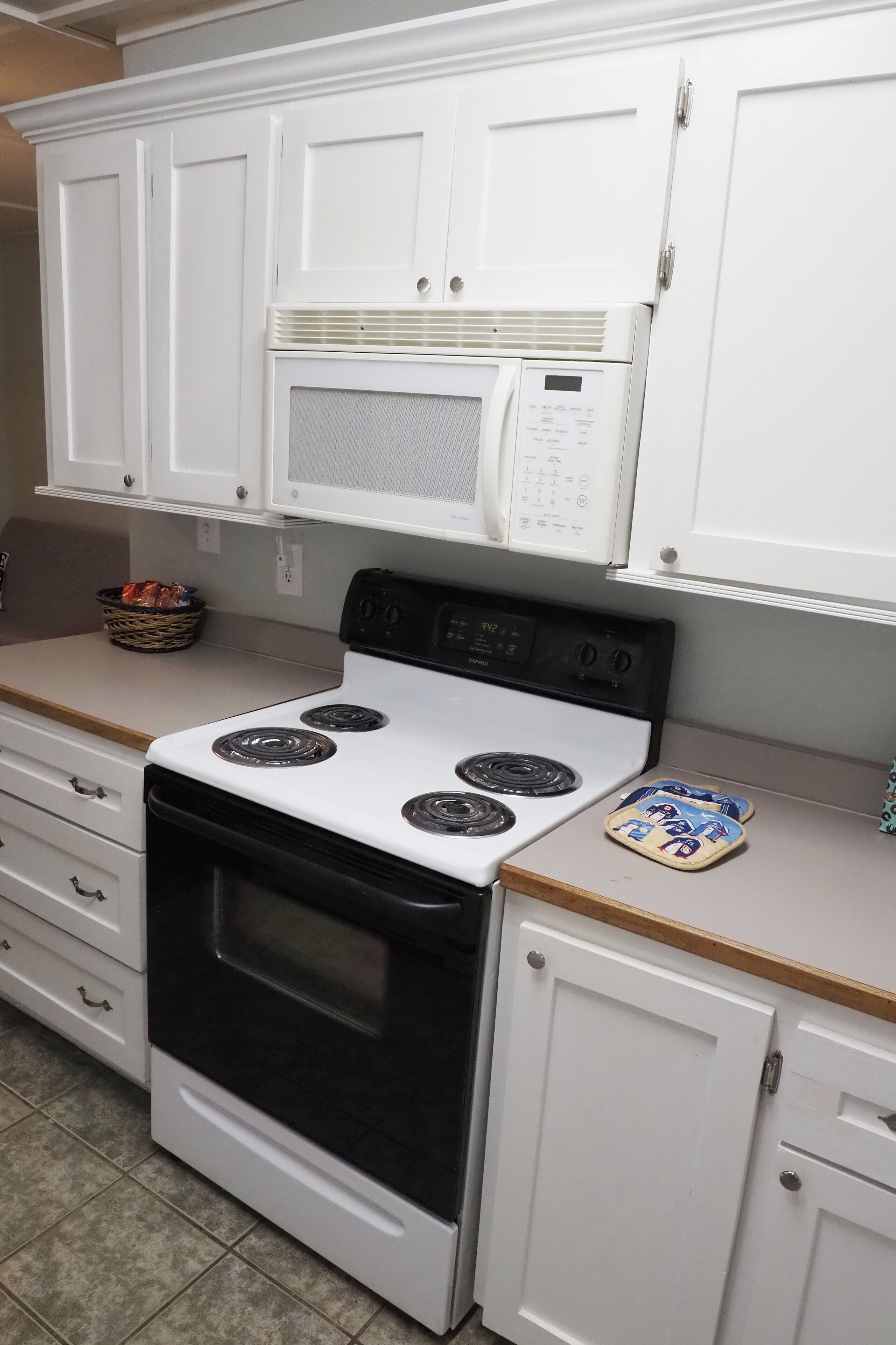 Una cocina con armarios blancos, una estufa, un microondas y un horno tostador.