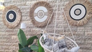 A room with a stone wall, a hanging macrame chair, a woven rug, and a potted plant.
