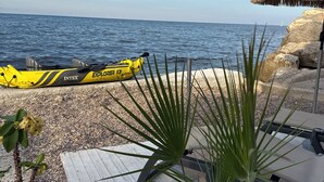 A beachside setting with a yellow inflatable boat, a thatched umbrella, and a wooden deck with lounge chairs.