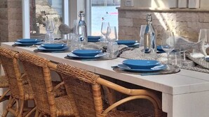 A dining area with a view of the sea, wicker chairs, and a table set with blue plates and glasses.
