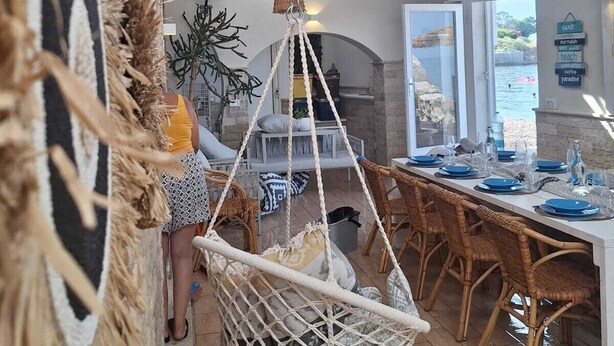 A dining area with a long table set for a meal, a hanging chair, and a fan in the background.