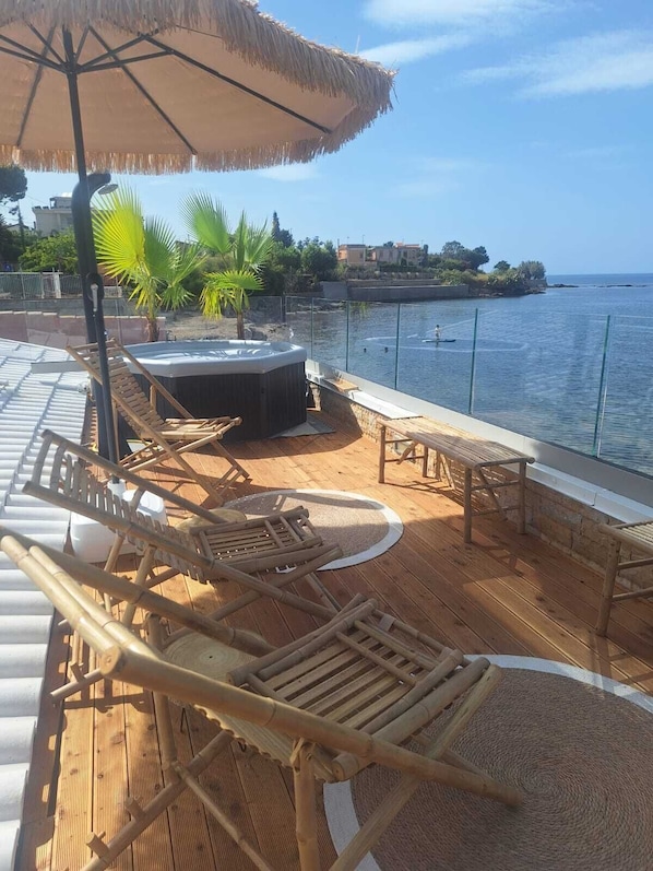 A wooden deck with lounge chairs and a hot tub overlooking a body of water. - Villa Teti: The Goddess of the Sea on the Beach (Trabia)