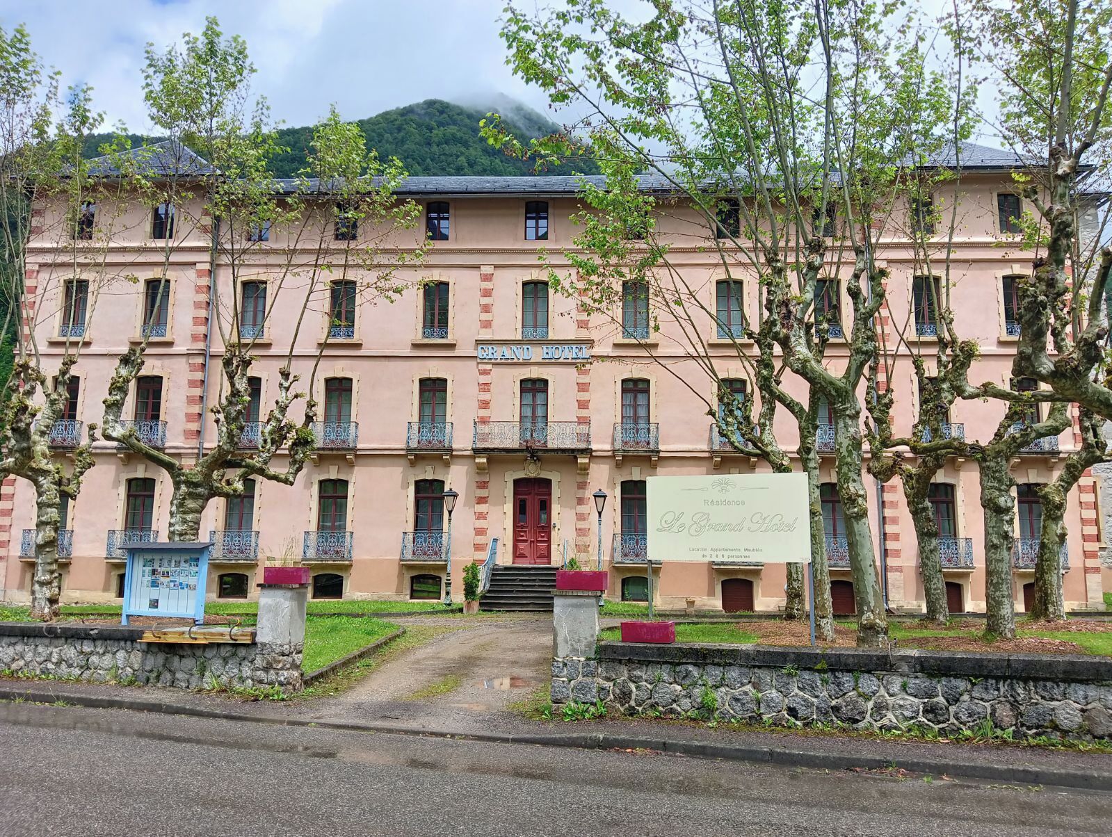 Un edificio rosa con balcones y una puerta roja, con el letrero 