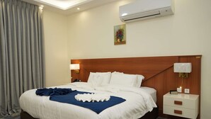 Habitación de hotel con una cama grande, cabecera de madera, mesita de noche con lámpara y unidad de aire acondicionado en la pared.