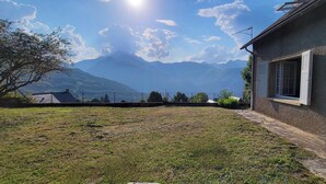 Une maison avec un chemin de pierre menant à l’entrée, une vue sur les montagnes et un ciel dégagé.
