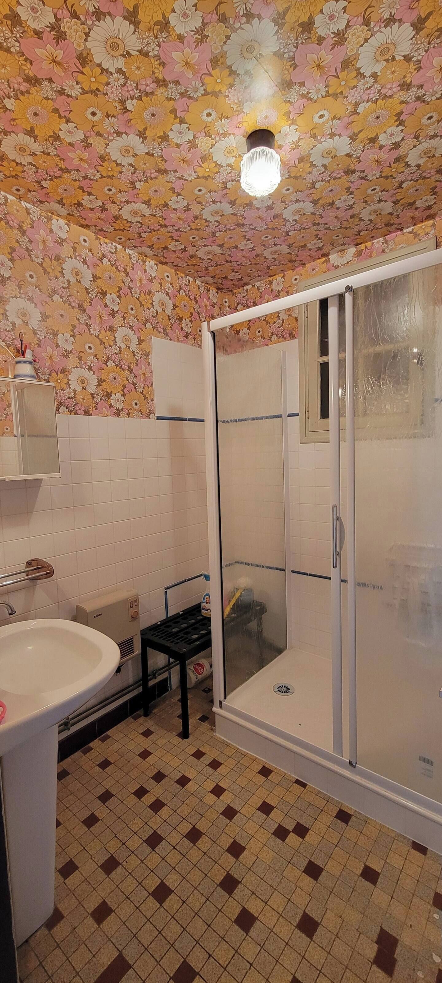 A bathroom with a floral ceiling, a shower with a glass door, a sink, and a tiled floor.